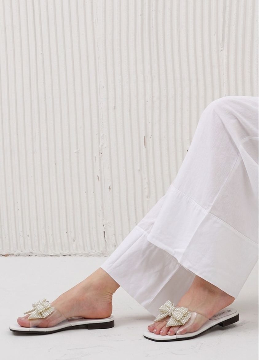 Person wearing white sandals with decorative straps on a light wooden floor.
