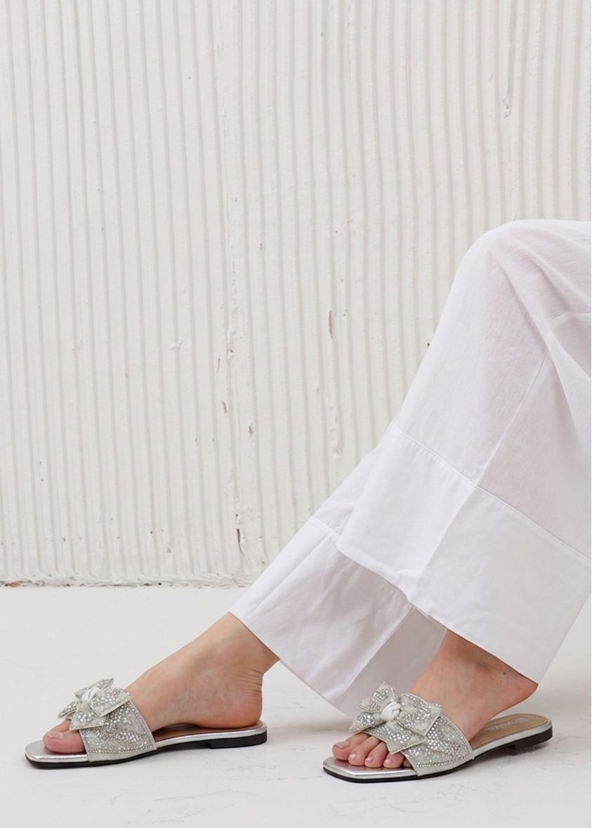 Silver sandals worn with white pants against a light background