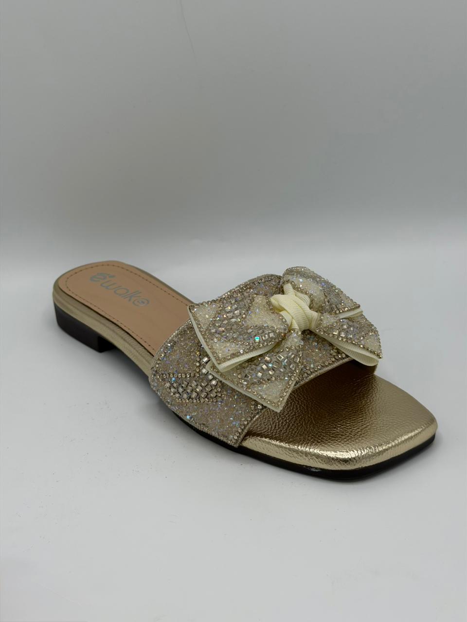 Gold sandal with bow detail on a gray background