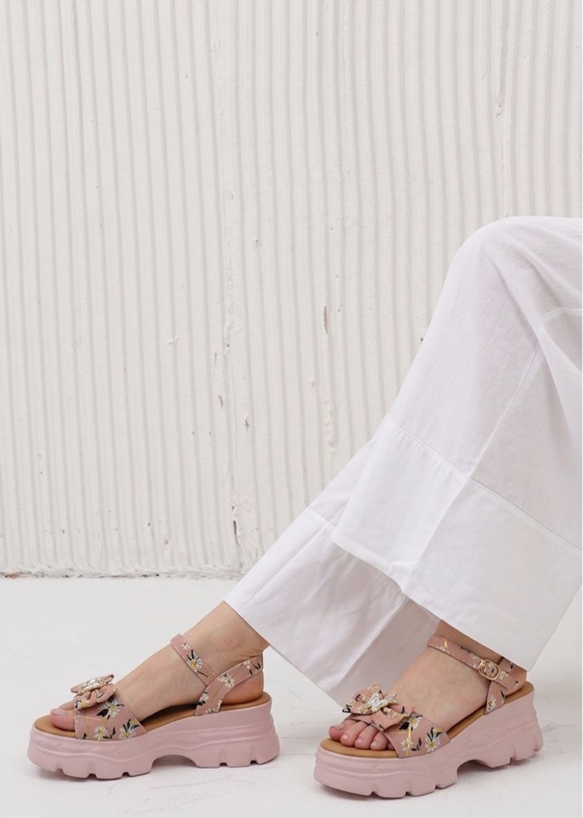 Pink sandals with floral details worn by a person sitting on a white surface.