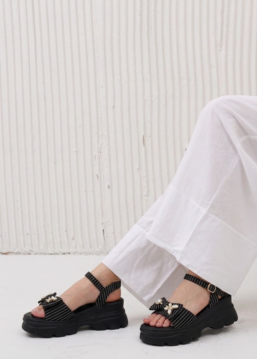 Black sandals worn with white pants against a light background