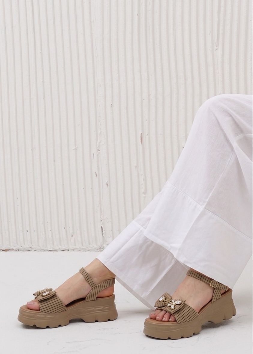 Brown sandals worn with white pants on a light background