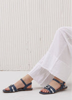 Navy sandals worn with white pants against a light wooden floor.