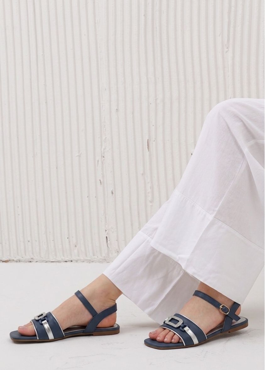 Navy sandals worn with white pants against a light wooden floor.