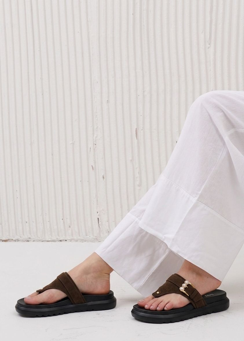Brown sandals worn with white pants against a light background
