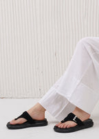 Person wearing black sandals and white pants against a light background