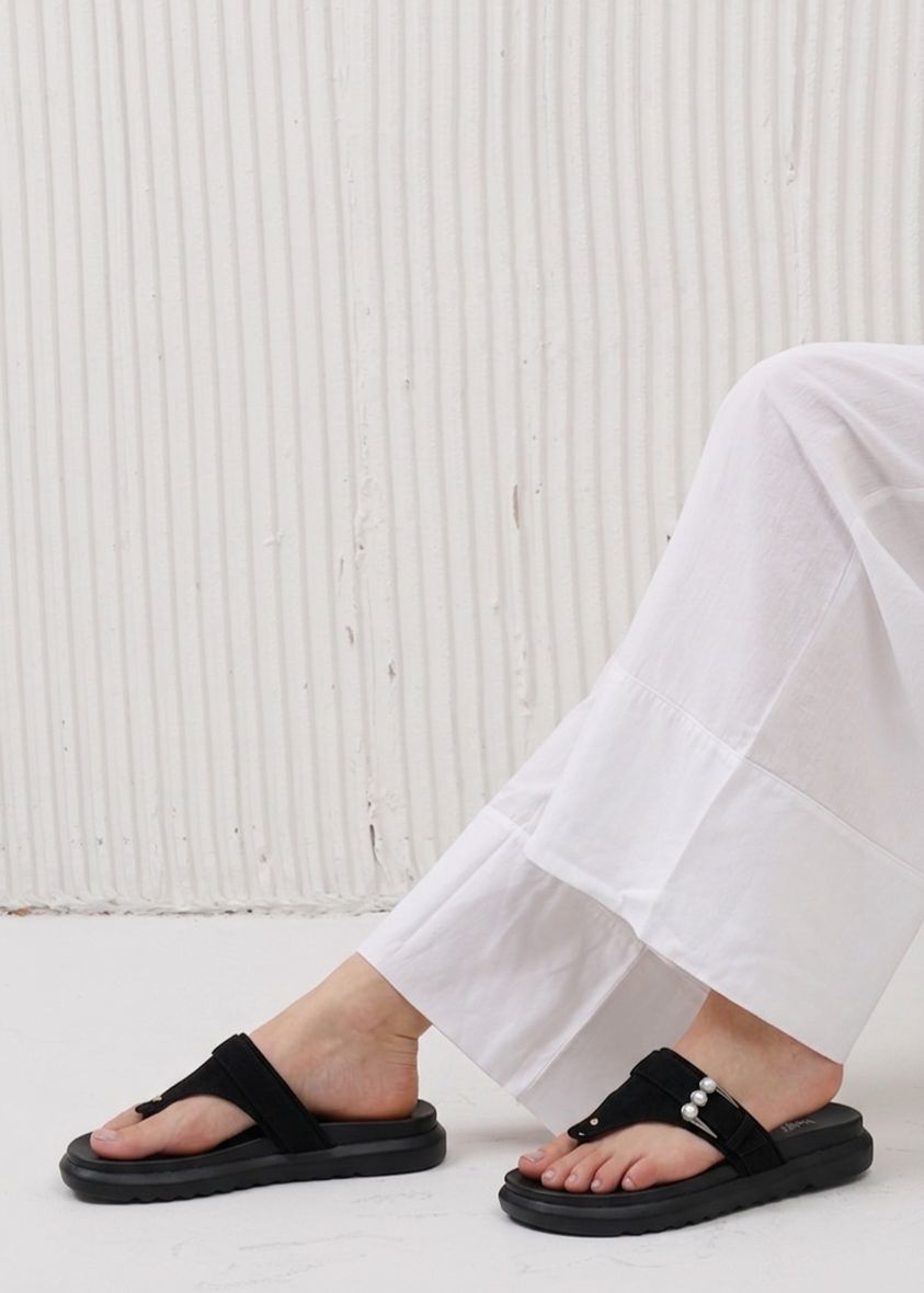 Person wearing black sandals and white pants against a light background