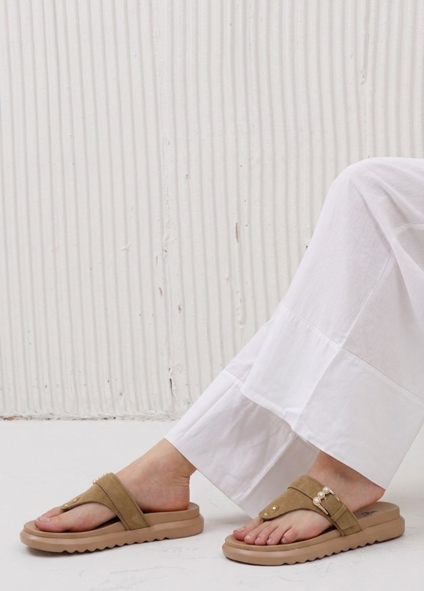 Brown sandals worn with white pants against a light background