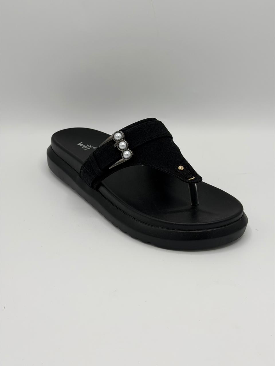 Black sandal with pearl embellishments on a gray background