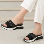 Black sandals with white soles worn by a person in white pants on a light background