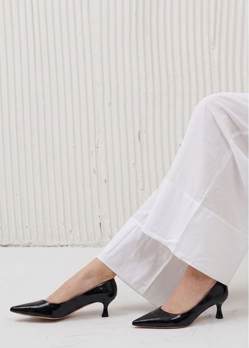 Person wearing black high heels and white pants against a light background