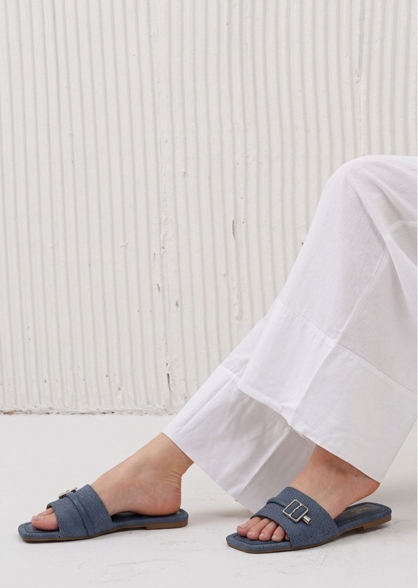 Person wearing blue sandals with a white textured wall background