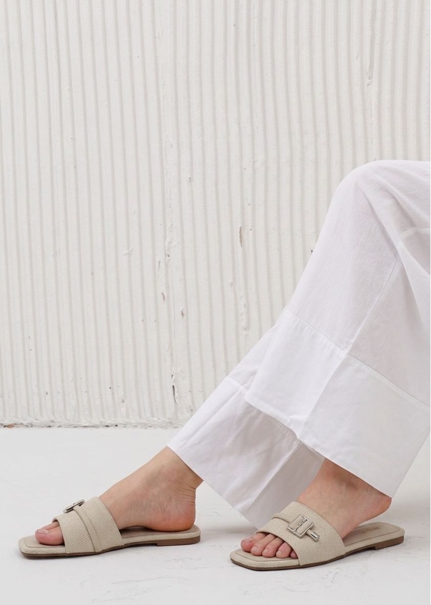Person wearing beige sandals and white pants against a light background