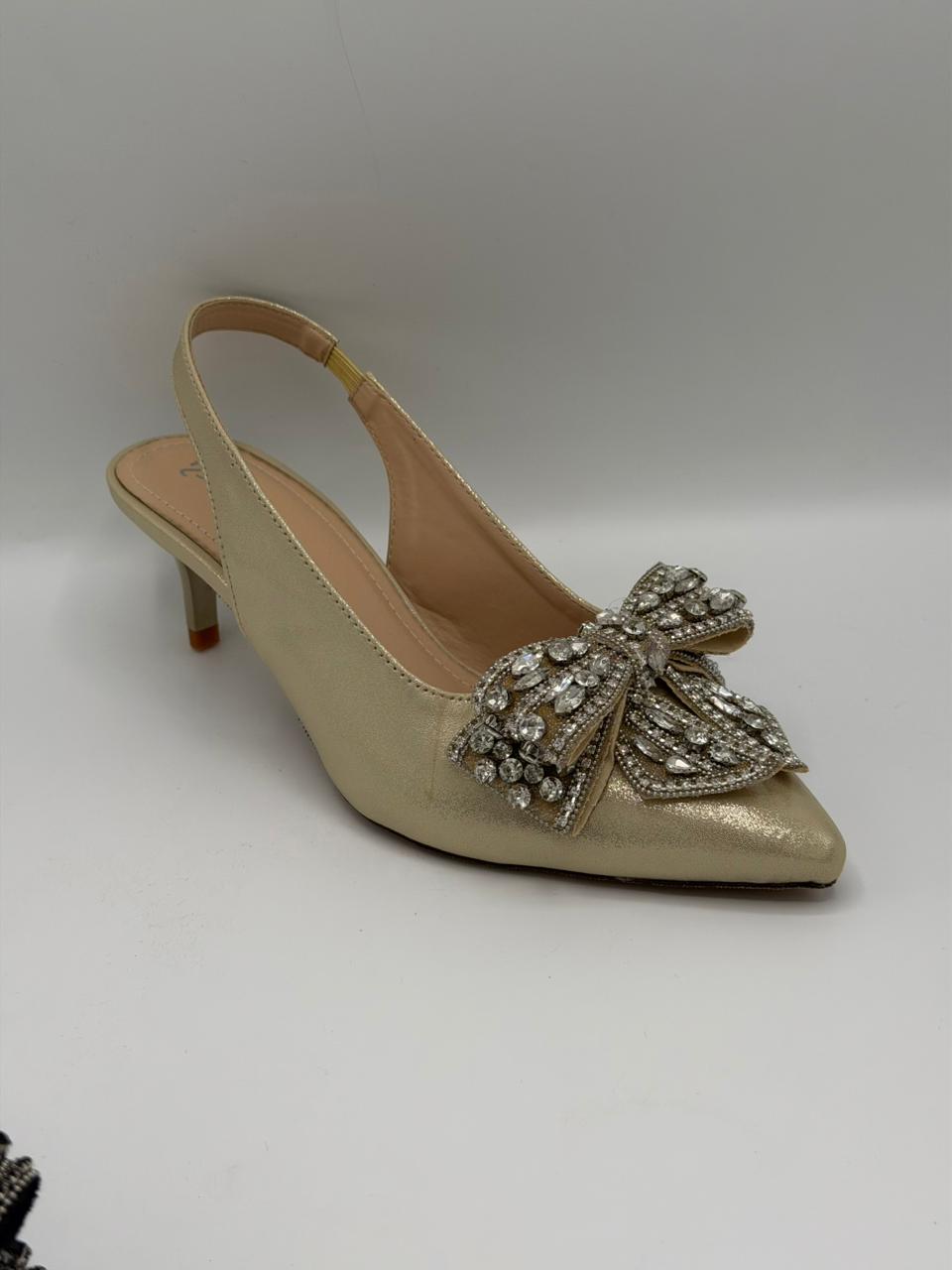 Gold high-heeled shoe with a decorative bow on a white background