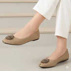 Beige flat shoes with floral embellishments worn by a person in white pants on a neutral background