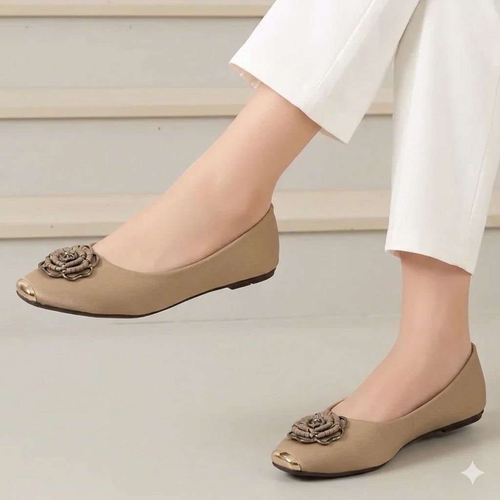 Beige flat shoes with floral embellishments worn by a person in white pants on a neutral background