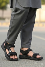 Person wearing black sandals and gray pants on a blurred street background