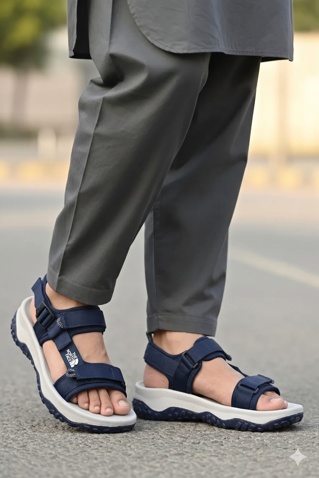 Person wearing navy sandals with white soles on a blurred street of the north face company background