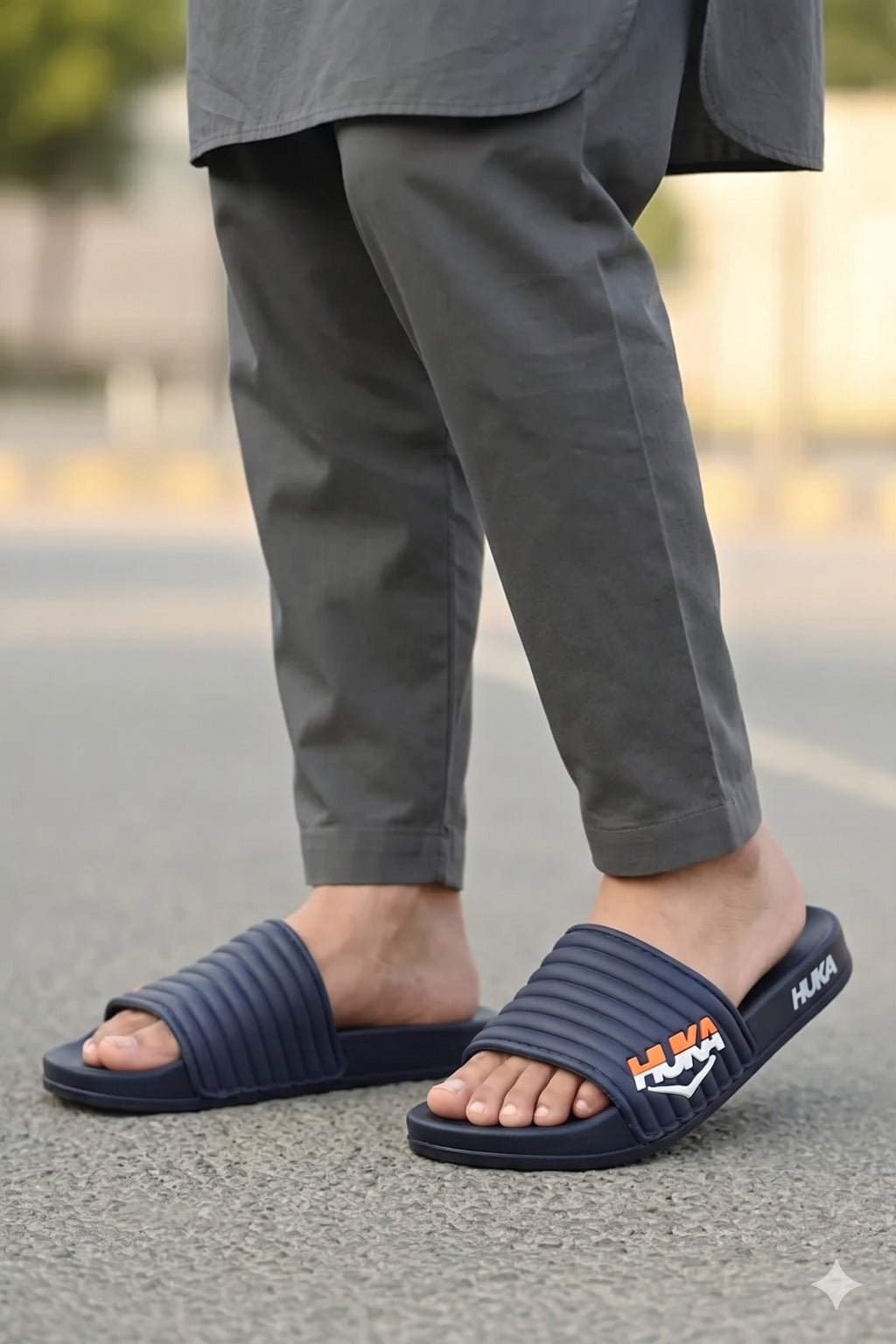 Person wearing navy slides with a logo Huka brand on a blurred outdoor background