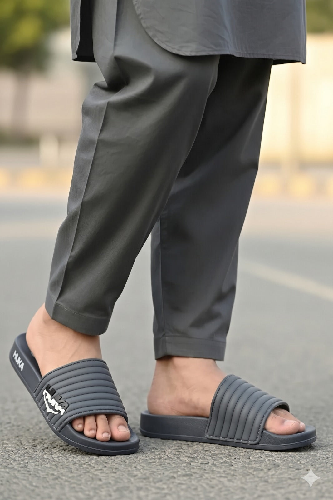 Person wearing gray sandals and pants on a blurred street background
