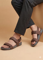 Brown sandals worn with dark pants on a beige background